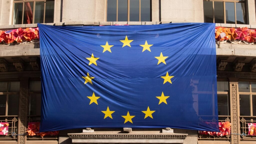 Large European Union flag draped over a building facade adorned with festive decorations.