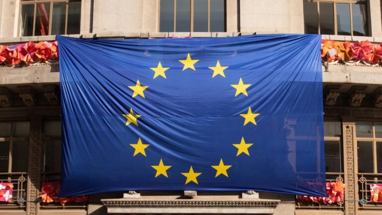 Large European Union flag draped over a building facade adorned with festive decorations.